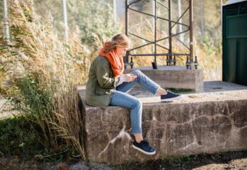 kvinna sitter på stenmur och tittar i mobil