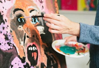 En hand håller i en pensel och målar ett porträtt