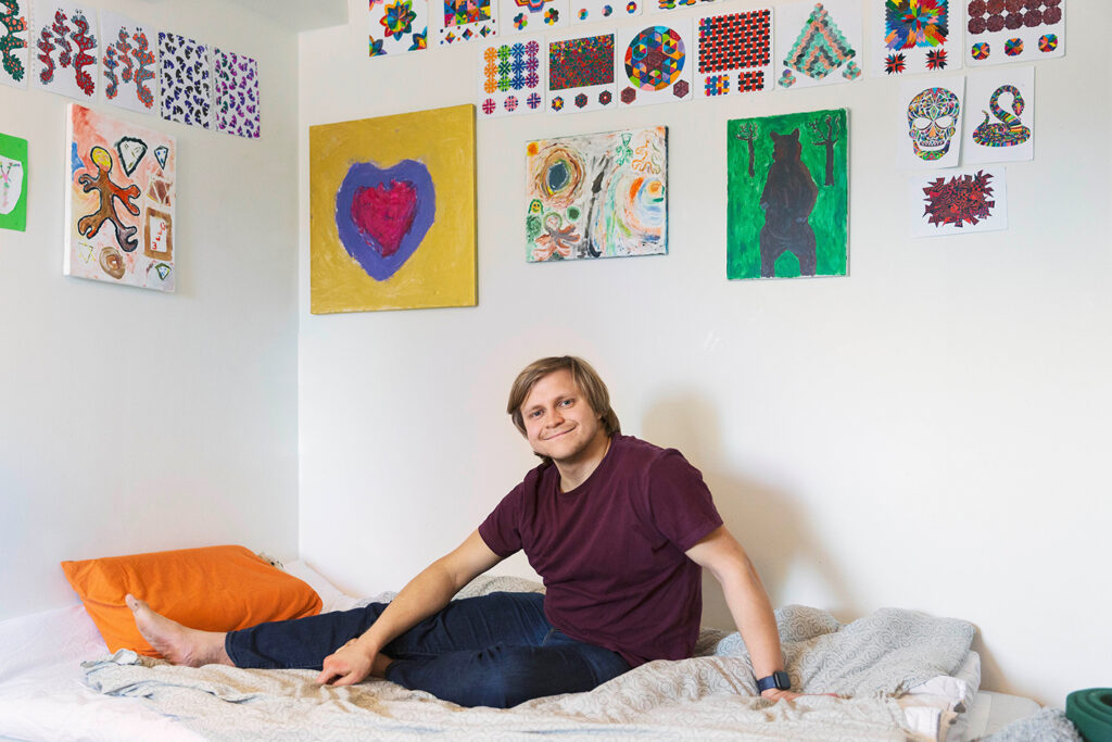 ung man sitter på säng på väggenegna målningar i olika färger