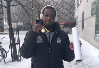 Mohammet utomhus med medalj runt halsen och affisch ihop rullad i handen
