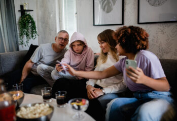 En familj sitter i soffa tittar på ett av barnens mobiler popcorn på bordet framför