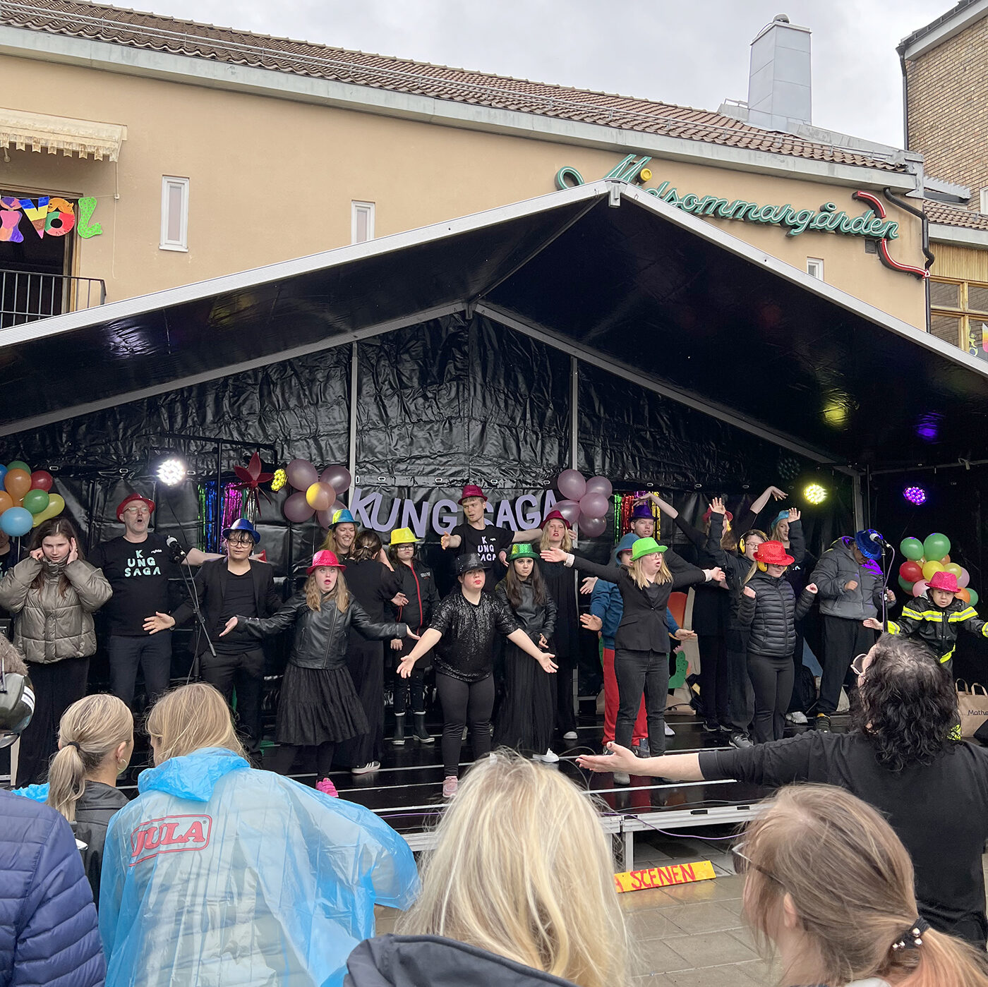 svart scen med svartklädd kör i förgrunden publik i regnkläder