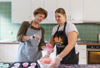 två kvinnor fyller rosa smet i formar på plåt