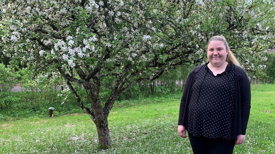 Sofie i svart tröja står i trädgården med blommande träd i bakgrunden