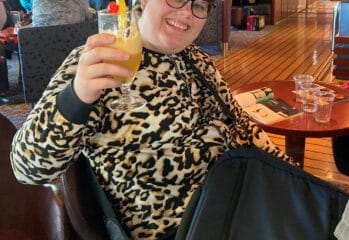 Natalie skålar mot kameran med drinkglas i handen