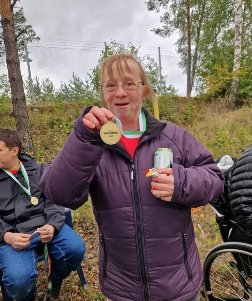 Stolt deltagare i lila jacka visar upp sin medalj