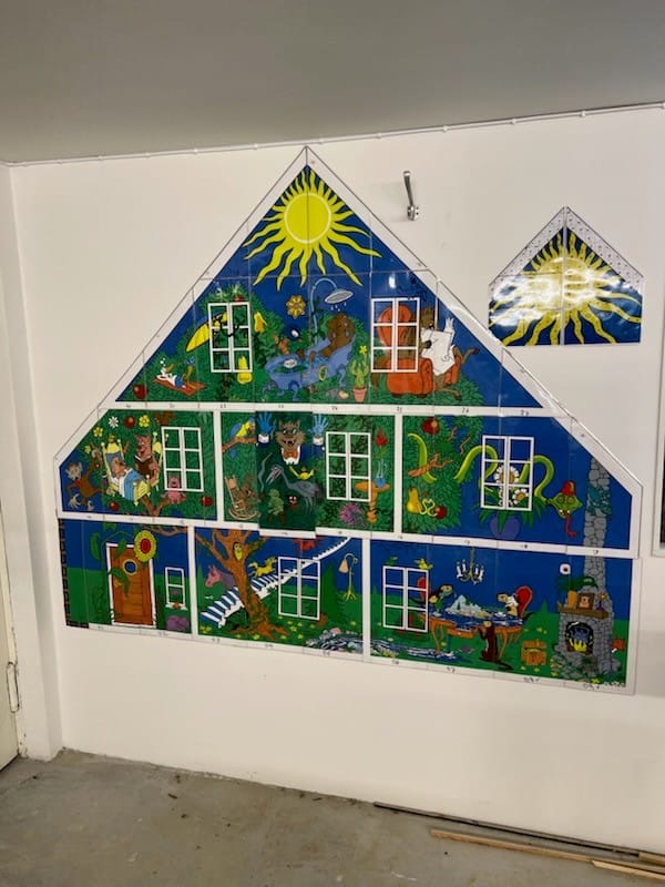 En stor väggmonterad konstinstallation formad som ett hus, uppdelad i flera rutor med färgglada illustrationer av djur, natur och fantasiscener.