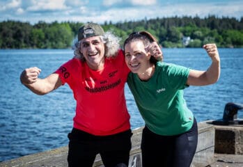 Salam och coach Caroline står vid vattnet, ler mot kameran och lyfter armarna i en peppande pose inför Glada Midnattsloppet.