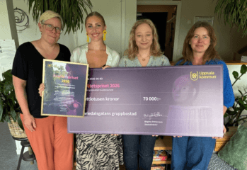 Fyra personer står inomhus och håller upp ett diplom och en stor prischeck från Uppsala kommun för Kvalitetspriset 2026. Checken är på 70 000 kronor och gäller Mariedalsgatans gruppbostad.
