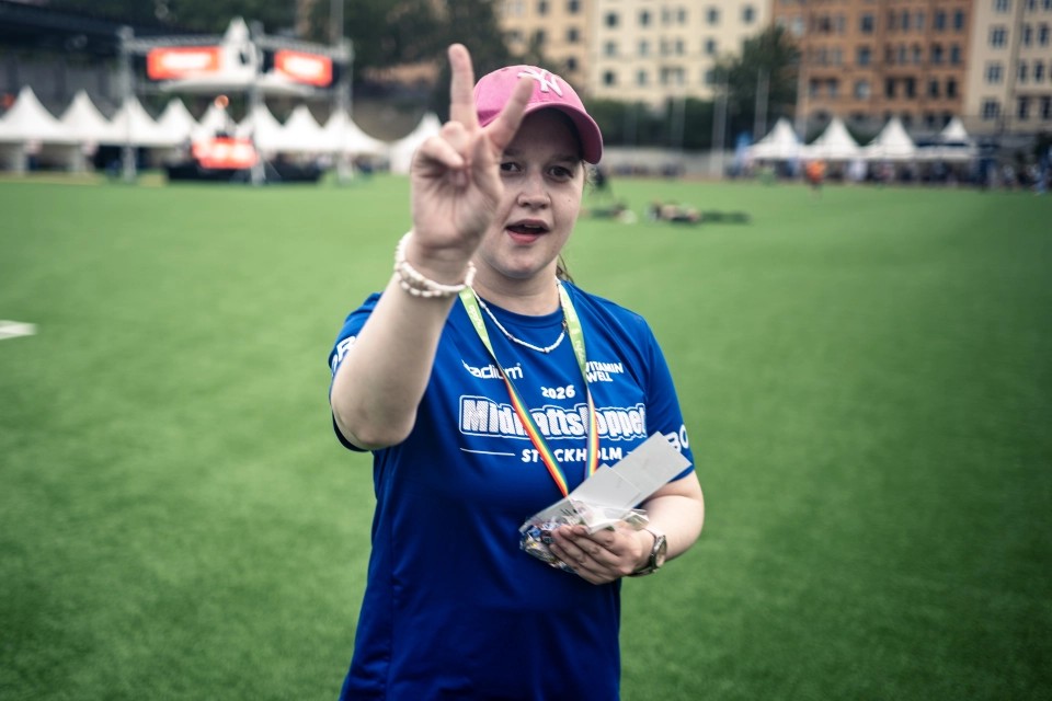 Person på en idrottsplan gör en V-gest och bär en tröja från Midnattsloppet Stockholm 2026.