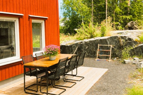 Uteplats med bord och stolar vid röd byggnad, med berg och grönska i bakgrunden.